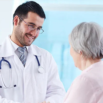 Doctor in white coat with stethoscope talking to a patient in a medical setting.