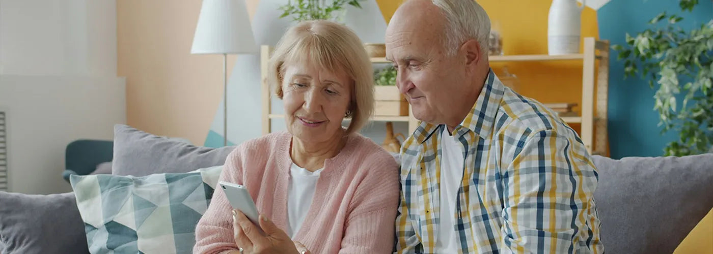 Older man and woman sitting on a couch looking at a phone together in a living room.