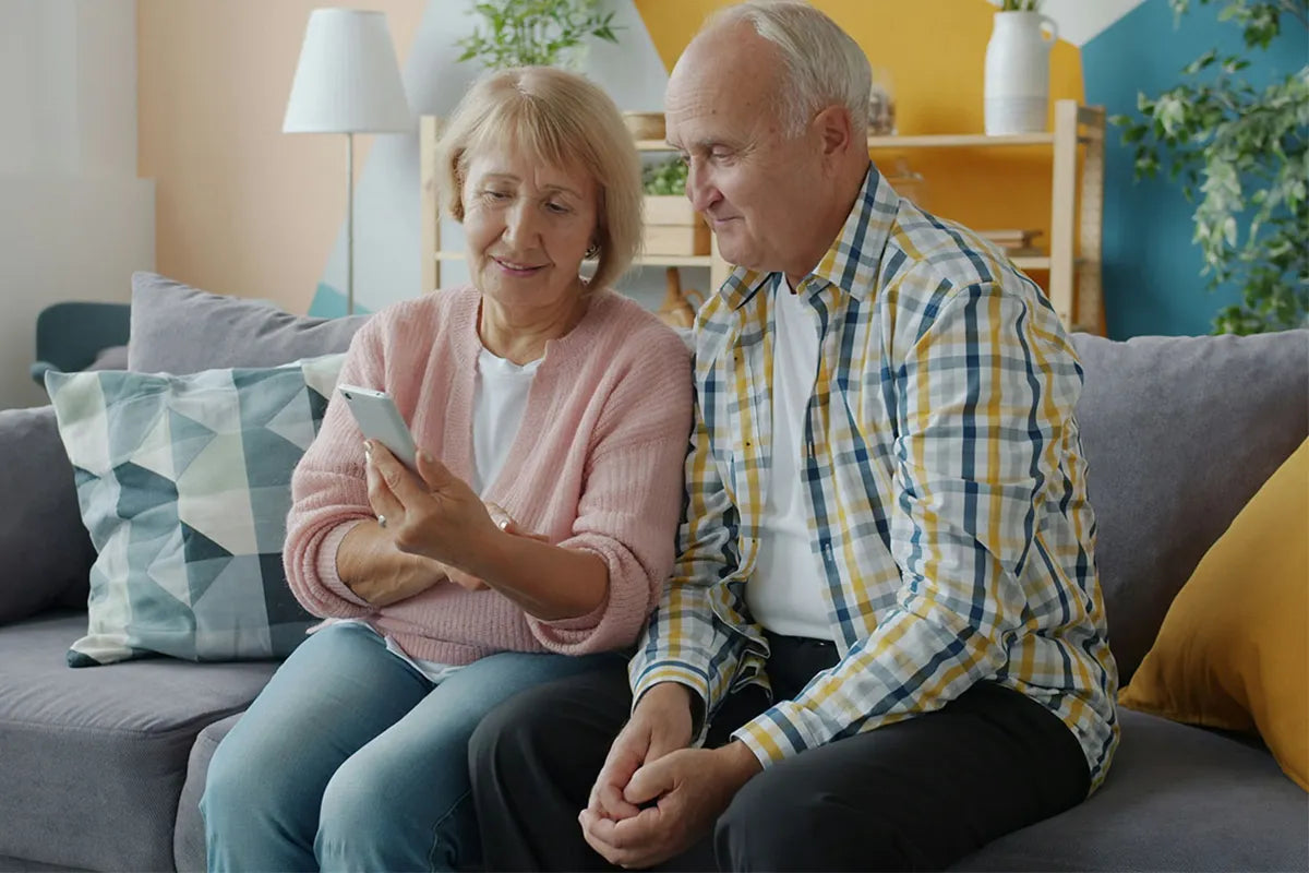 Senior couple sitting on a couch, looking at a smartphone together.