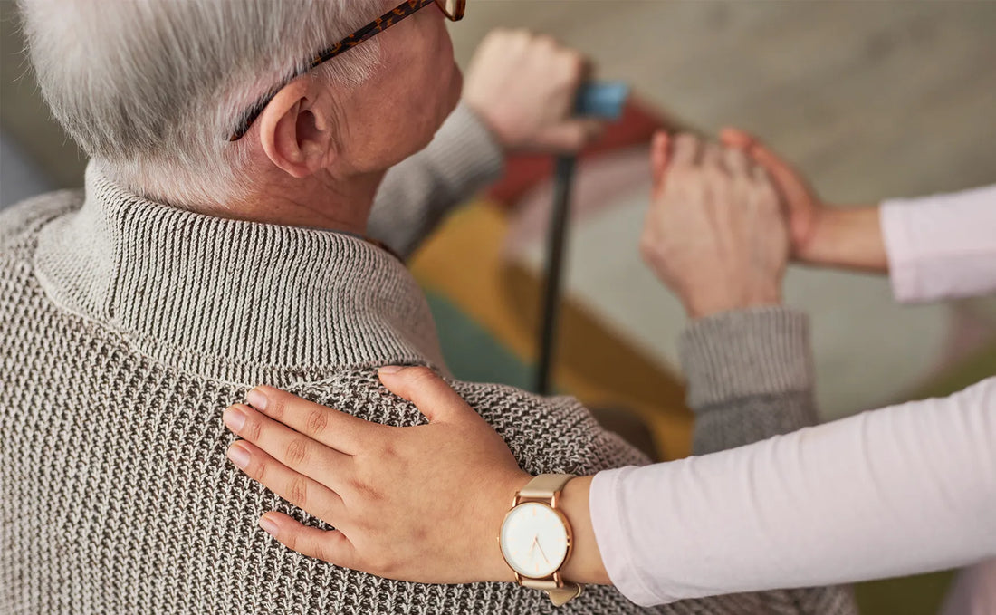 Old man facing away with caregiver's hand on his shoulder.