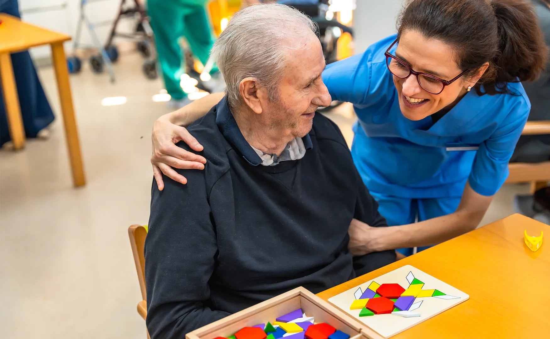 Caregiver assisting an elderly man with a colorful puzzle in a healthcare setting.